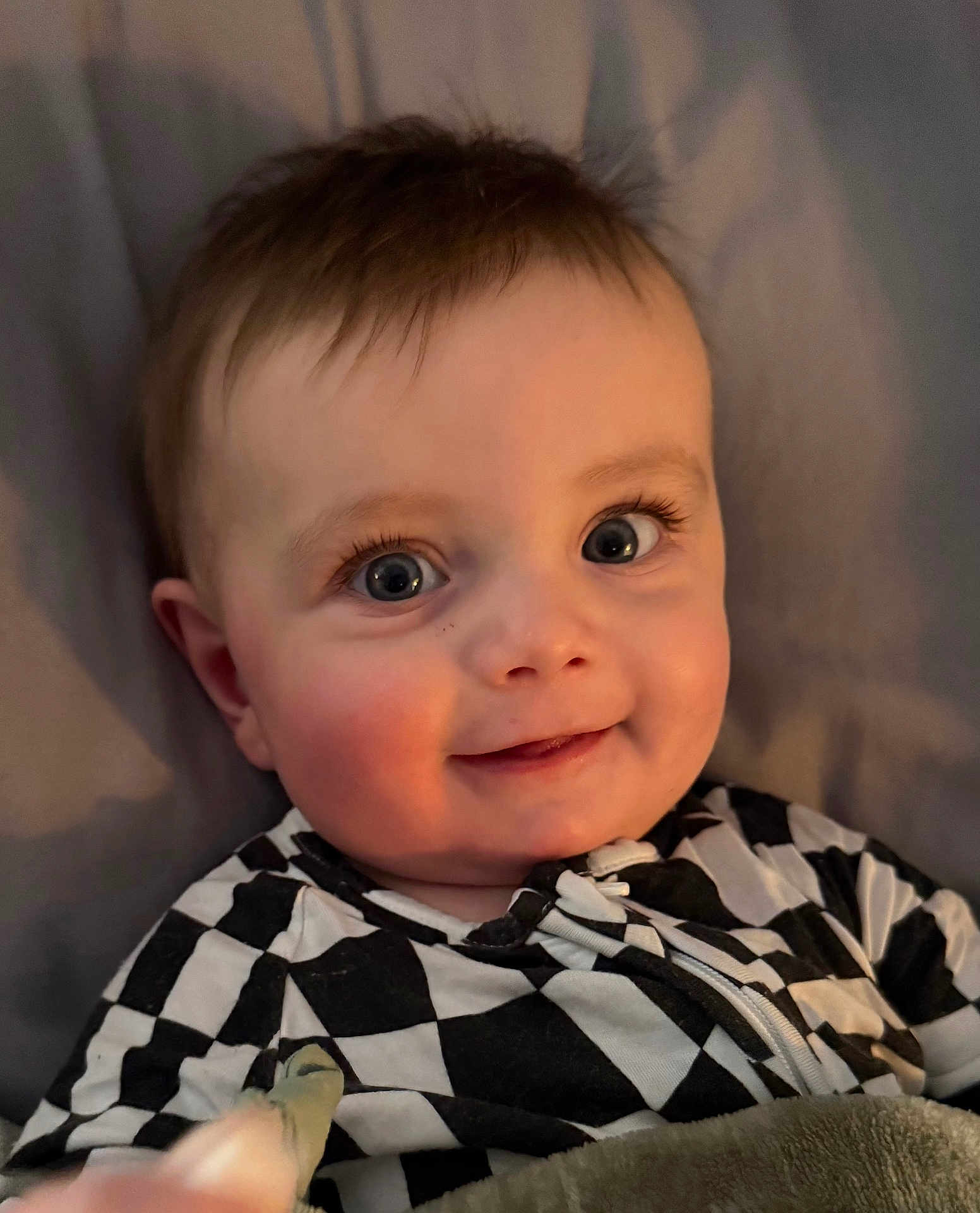 Colt joined the competition — help win amazing prizes! baby, infant, smiling, blue_eyes, long_eyelashes, rosy_cheeks, onesie, checker_pattern, blanket, closeup, portrait, bedroom, gaze, small_hands, hair, cute, sleepwear, laying_down, soft_light, happy