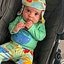 baby, child, stroller, hat, colorful_clothing, fish_print, palm_tree_print, infant, cute, indoors, seated, looking_at_camera, hand_near_mouth, foot, headwear, fabric, patterned_clothes, person, casual_wear, soft_lighting