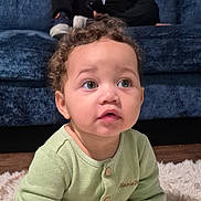 Matias joined the competition — help win amazing prizes! baby, child, infant, curly_hair, wide_eyes, surprised, sitting, portrait, close_up, face, green_outfit, buttoned_shirt, blue_couch, fluffy_rug, indoor, home, wood_floor, photography, cute, adorable