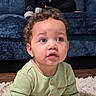 baby, child, infant, curly_hair, wide_eyes, surprised, sitting, portrait, close_up, face, green_outfit, buttoned_shirt, blue_couch, fluffy_rug, indoor, home, wood_floor, photography, cute, adorable