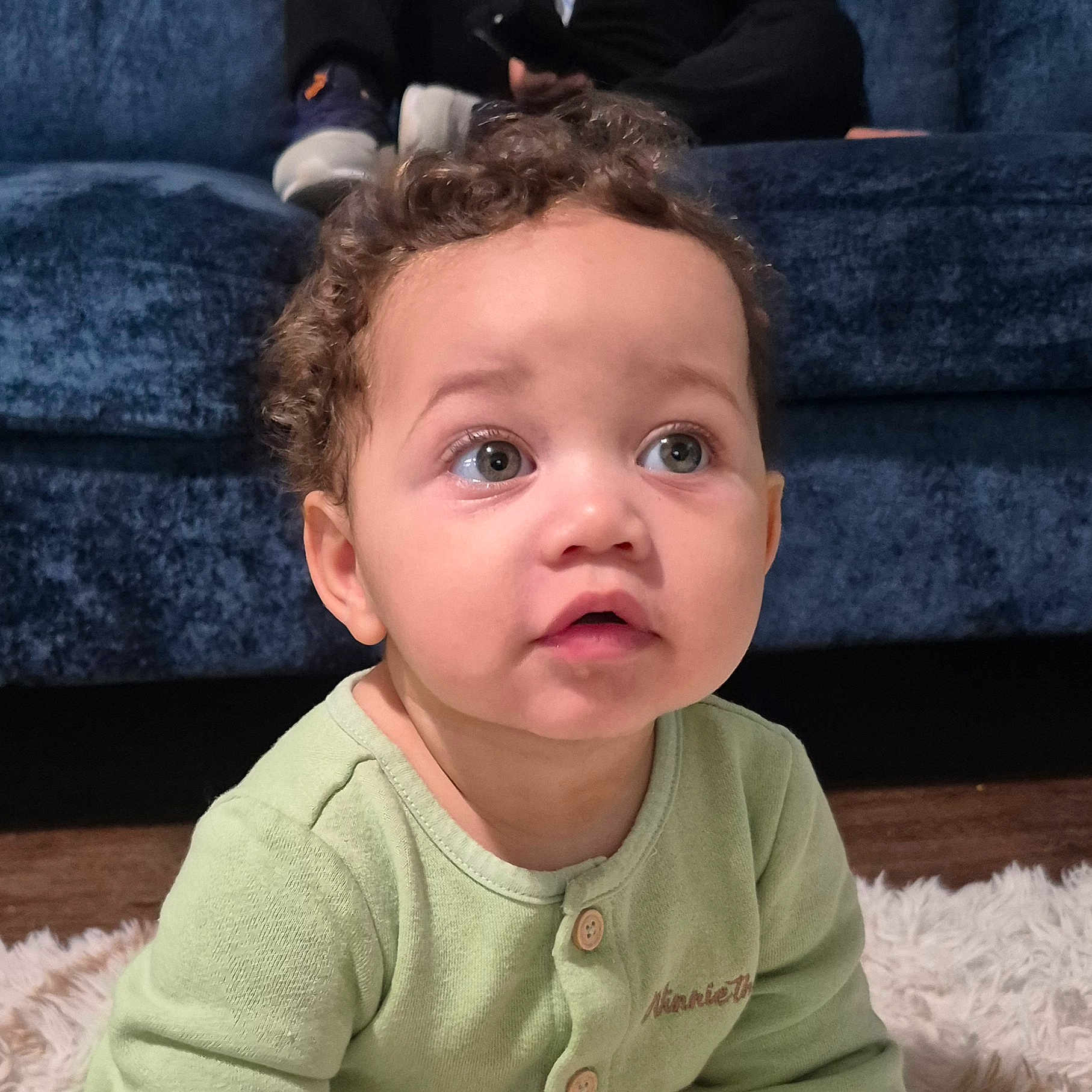 Matias joined the competition — help win amazing prizes! baby, child, infant, curly_hair, wide_eyes, surprised, sitting, portrait, close_up, face, green_outfit, buttoned_shirt, blue_couch, fluffy_rug, indoor, home, wood_floor, photography, cute, adorable