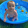 baby, child, pool, water, toys, blue_pool, outdoor, grass, summer, play, wet, curious, kneeling, toy_ball, toy_duck, toy_rings, barefoot, innocent, face, person