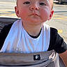 baby, child, infant, portrait, face, serious, looking_at_camera, bib, black_shirt, sitting, outdoor, sunlight, street, car, red_car, vehicle, picnic_table, wood, photography, close_up