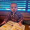 baby, child, infant, portrait, sitting, table, restaurant, menu, food, hands, wide_eyes, open_mouth, curious, patterned_clothing, onesie, indoor, window, blinds, wood, photography
