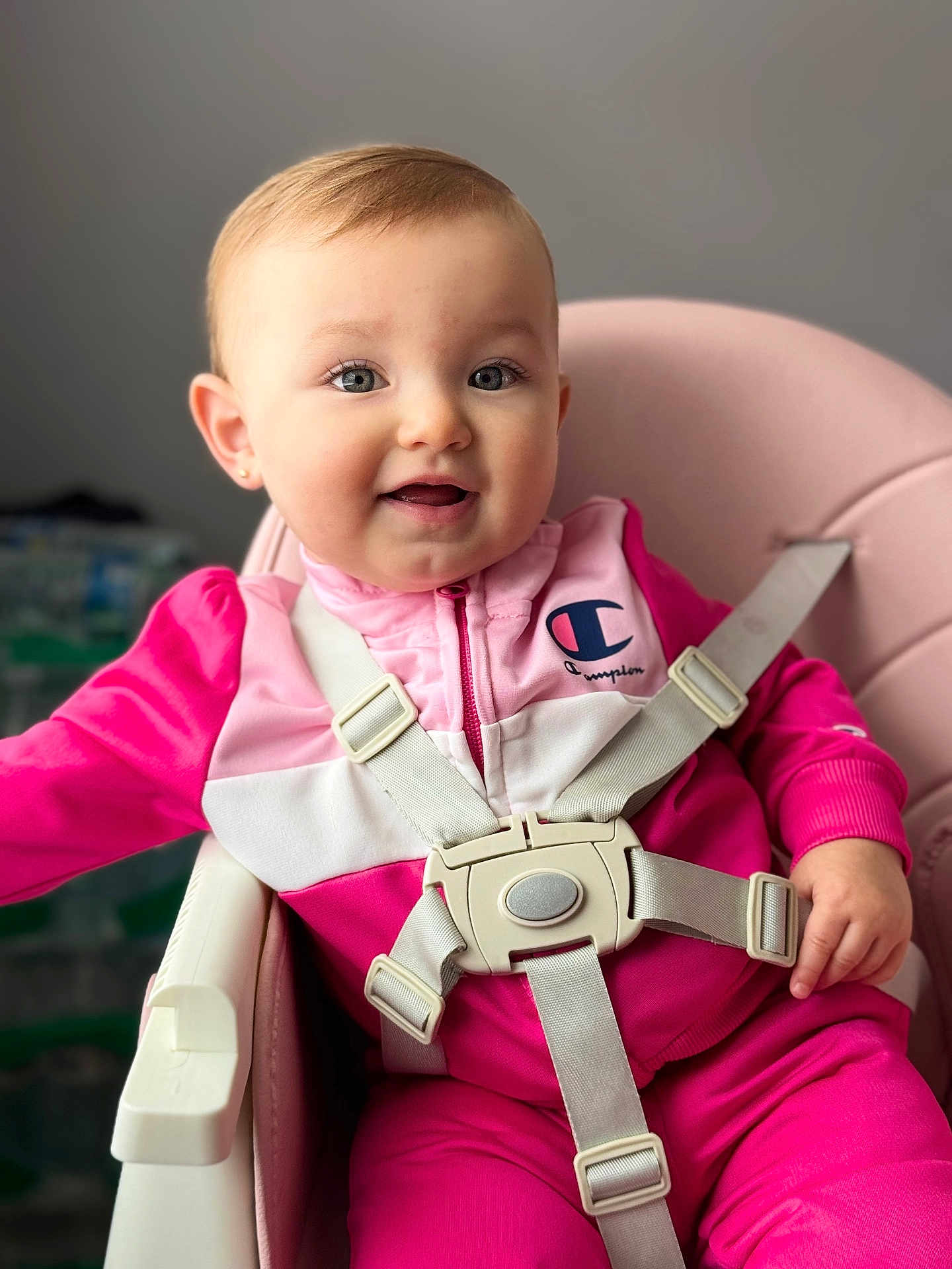 Adele joined the competition — help win amazing prizes! baby, child, pink_clothing, high_chair, smile, face, eyes, earring, seatbelt, indoor, person, happy, infant, cute, portrait, soft_lighting, young_child, jacket, zipper, closeup