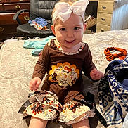 Haizelee is registered to the contest to win money with this photo: baby, child, sitting, bed, headband, bow, turkey, clothing, pattern, room, chair, dresser, foot, happy, smiling, indoors, furniture, textile, blanket, person