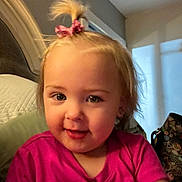Ryleigh is registered to the contest to win money with this photo: child, toddler, portrait, smiling, pink_shirt, hair_bow, blonde_hair, blue_eyes, rosy_cheeks, sitting, couch, cushion, indoors, home, warm_lighting, close_up, face, baby, happy, photograph