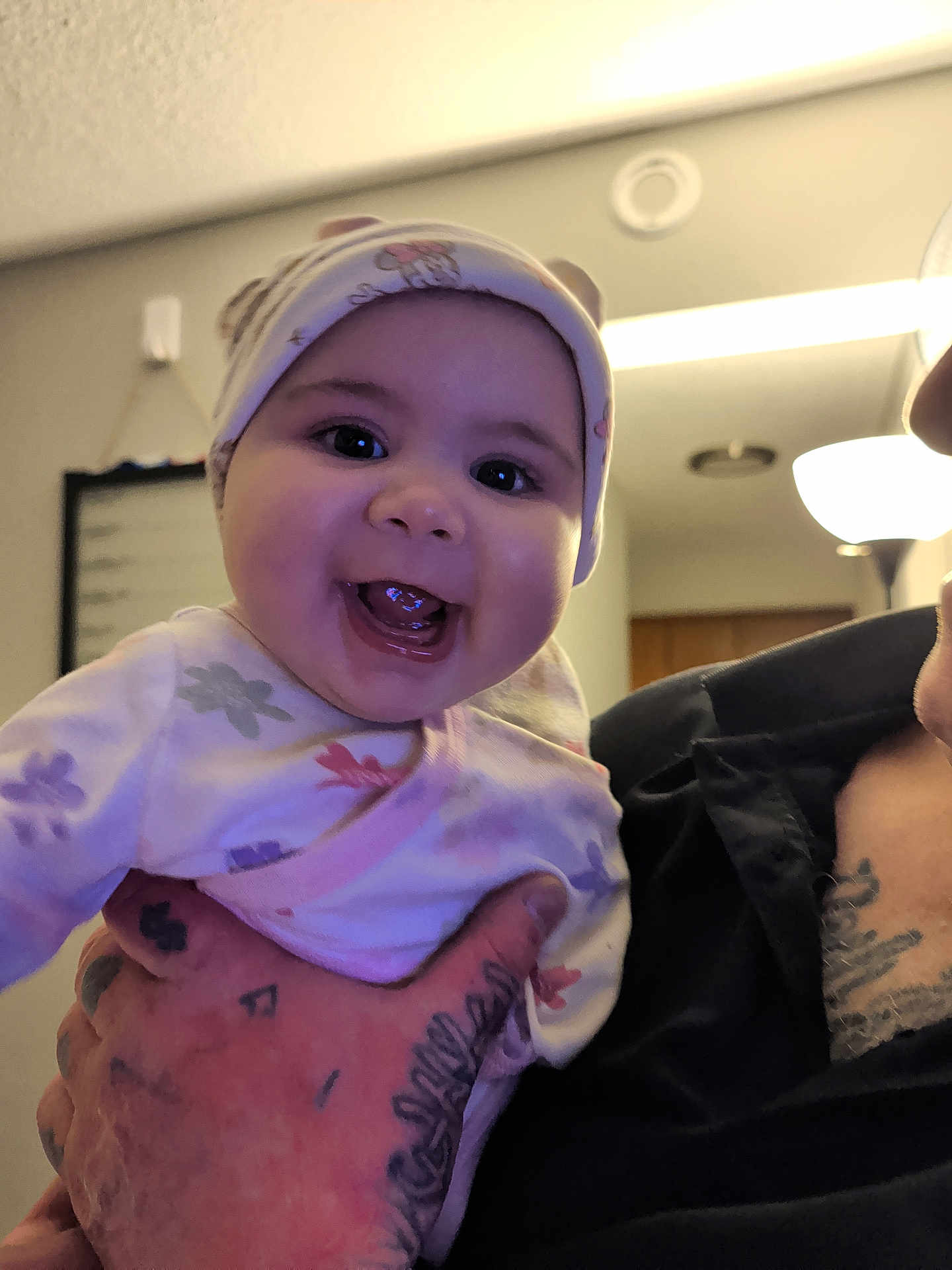 Aiyah is registered to the contest to win money with this photo: baby, smiling, infant, person, hand, tattoo, indoor, lamp, ceiling, clothing, hat, face, happy, holding, portrait, cute, child, room, adult, background