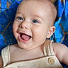 Dylan is registered to the contest to win money with this photo: baby, child, infant, smiling, laughing, portrait, face, eyes, tongue, happy, joyful, lying_down, blue_blanket, patterned_fabric, overalls, clothing, button, indoor, close_up, photography