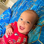 Dylan joined the competition — help win amazing prizes! baby, infant, child, smiling, happy, portrait, close_up, lying_down, red_outfit, blue_blanket, patterned_fabric, racing_cars, car_print, indoors, bedroom, cozy, bright_colors, open_mouth, blue_eyes, happy_expression