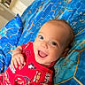 baby, infant, child, smiling, happy, portrait, close_up, lying_down, red_outfit, blue_blanket, patterned_fabric, racing_cars, car_print, indoors, bedroom, cozy, bright_colors, open_mouth, blue_eyes, happy_expression
