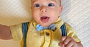 Dylan joined the competition — help win amazing prizes! baby, child, infant, portrait, lying_down, indoors, mattress, quilted, yellow_shirt, bow_tie, suspenders, blue_pants, brown_buttons, wide_eyes, open_mouth, smiling, hand, arm, fashion, close_up