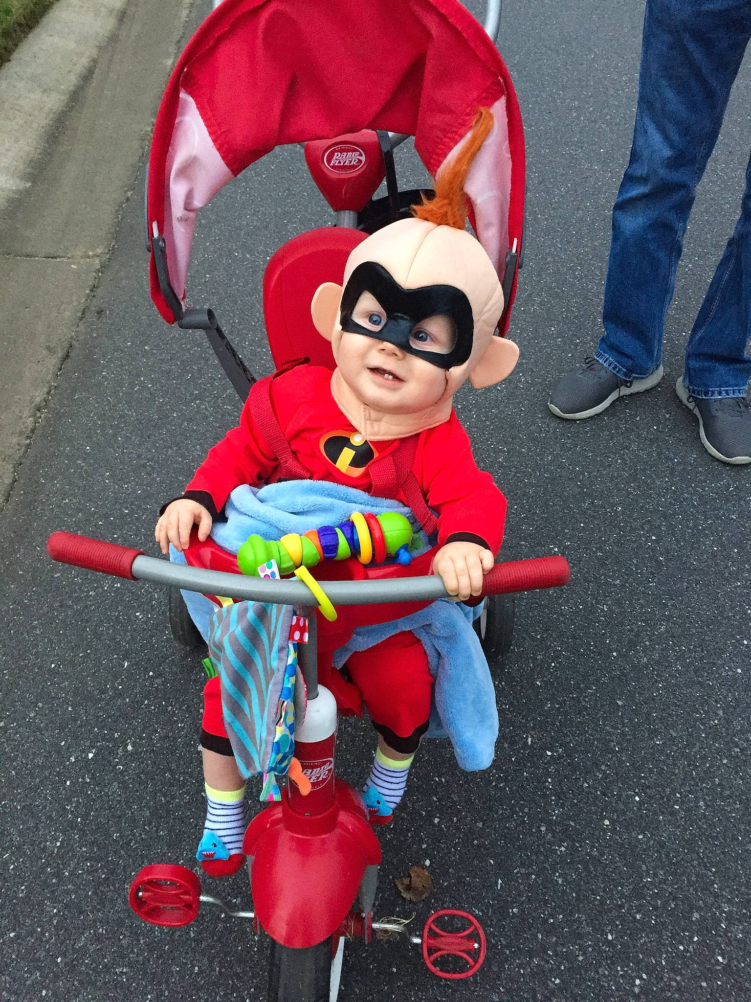 Brixton is registered to the contest to win money with this photo: baby_products, boot, chair, child, electric_blue, fictional_character, footwear, fun, justice_league, person, personal_protective_equipment, public_space, recreation, shoe, sitting, sneakers, tire, toddler, toy, tricycle