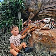 Jordan joined the competition — help win amazing prizes! toddler, child, dragon, dinosaur, sculpture, toy, nature, plants, greenery, camouflage, rock, outdoor, happy, smiling, shorts, tshirt, shoes, curly_hair, play, fantasy