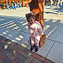 toddler, child, pink_clothing, sneakers, wooden_post, outdoor, sunlight, shadows, concrete, brick_pavement, people, park, trees, decorations, daytime, playful, smiling, cute, casual_wear, public_space