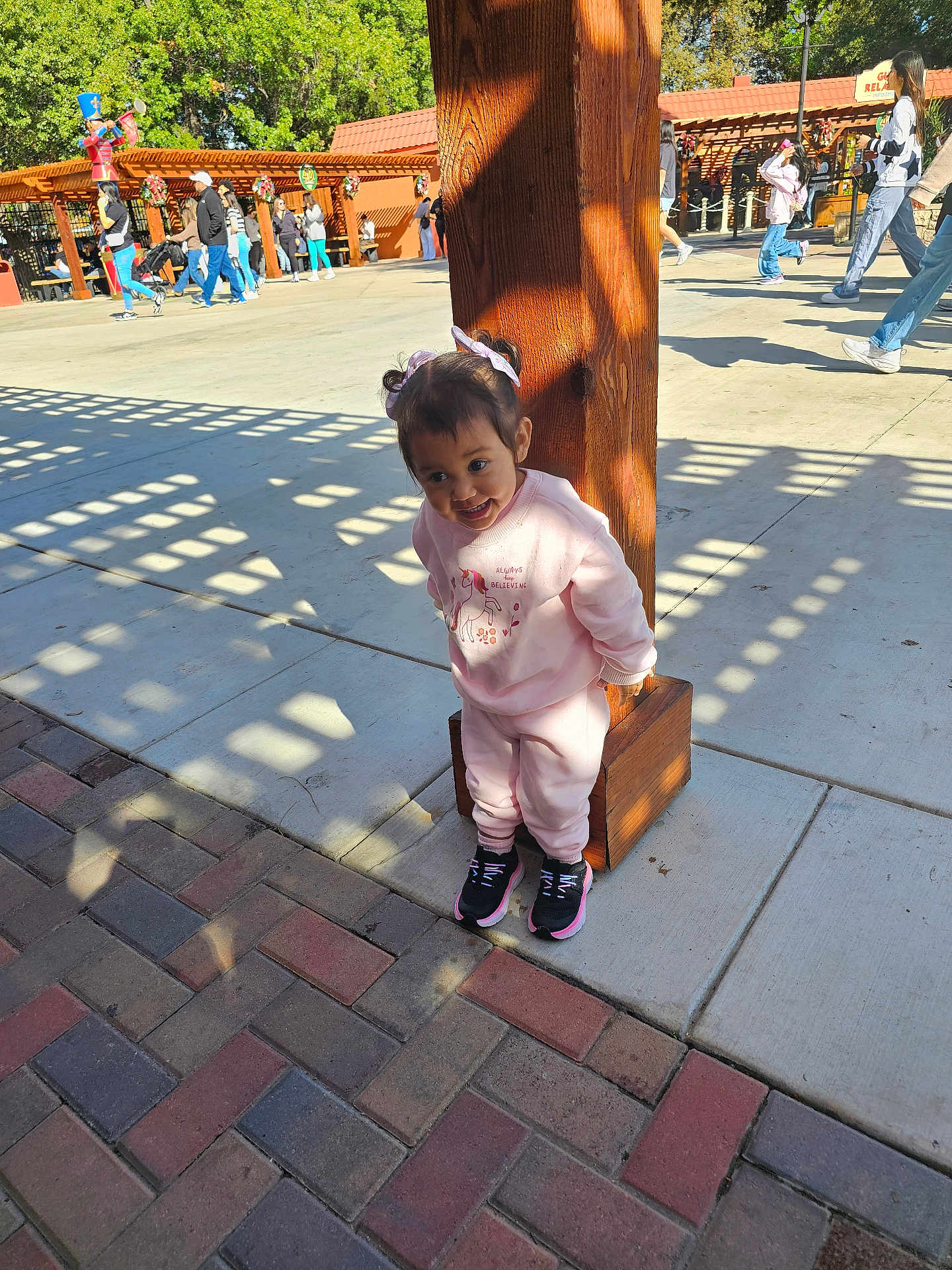 Eliana joined the competition — help win amazing prizes! toddler, child, pink_clothing, sneakers, wooden_post, outdoor, sunlight, shadows, concrete, brick_pavement, people, park, trees, decorations, daytime, playful, smiling, cute, casual_wear, public_space