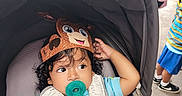 Emiliano is registered to the contest to win money with this photo: baby, blue_shirt, car_seat, child, children, crown, curly_hair, daylight, family, harness, infant, monkey_crown, outdoor, pacifier, photography, playground, portrait, sitting, smiling, stroller