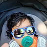 adorable, baby, baby_accessories, car_seat, child, close_up, curly_hair, dark_hair, face, gray_clothing, infant, orange_clothing, pacifier, portrait, reflection, seated, sunglasses, sunlight, travel, vehicle_interior