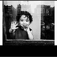 Julian is registered to the contest to win money with this photo: child, toddler, black_and_white, window, reflection, smile, hand, face, curly_hair, urban, buildings, glass, portrait, greeting, young_child, monochrome, cute, happy, indoors, casual
