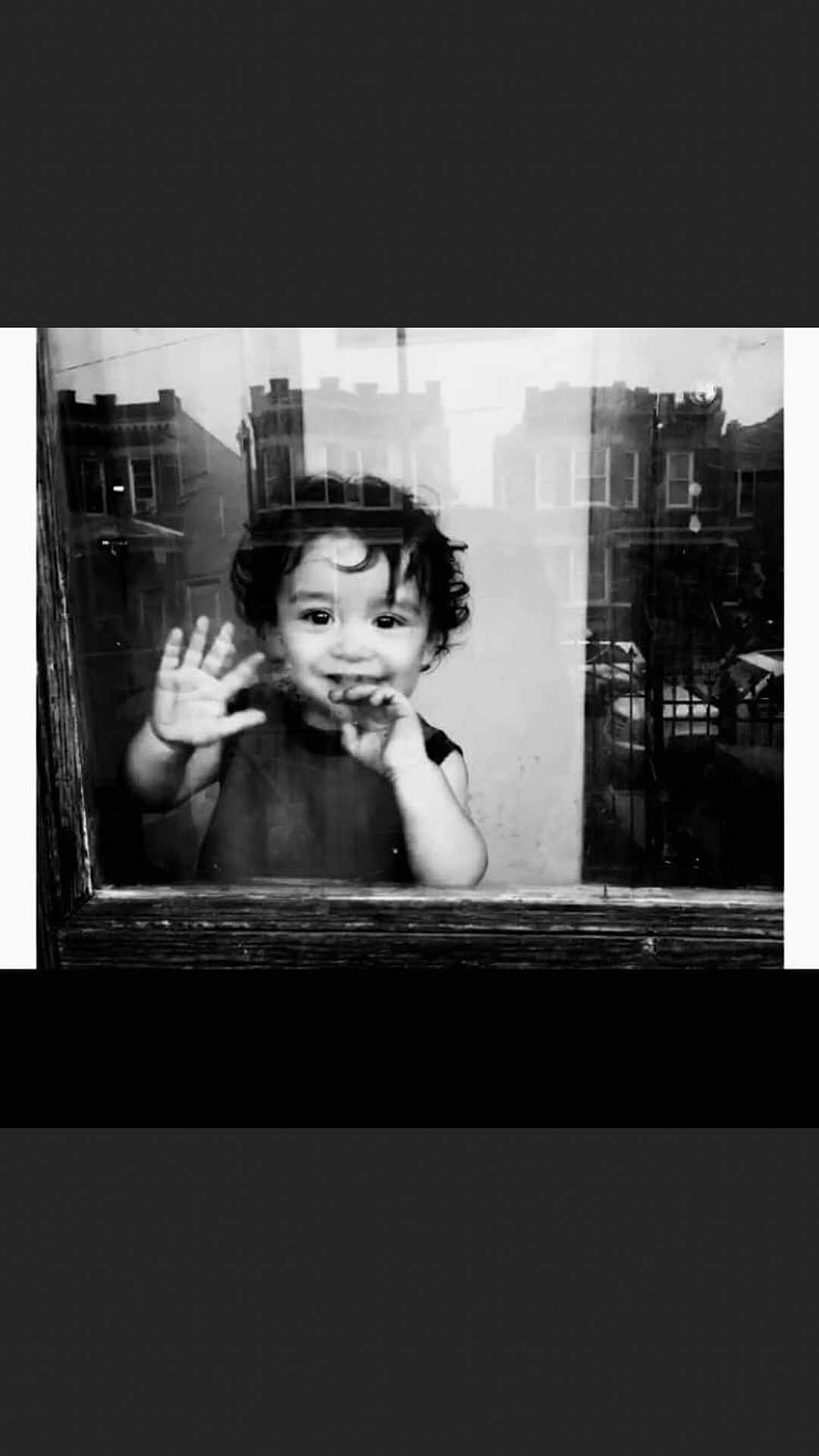 Julian is registered to the contest to win money with this photo: child, toddler, black_and_white, window, reflection, smile, hand, face, curly_hair, urban, buildings, glass, portrait, greeting, young_child, monochrome, cute, happy, indoors, casual