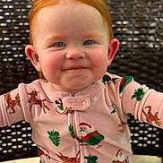 Elsie is registered to the contest to win money with this photo: baby, child, red_hair, smile, face, pajamas, christmas_theme, santa, reindeer, chair, woven_chair, happy, cute, portrait, indoors, infant, holiday, seasonal_clothing, person, young_child