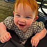 toddler, child, red_hair, blue_eyes, smiling, happy, baby, face, portrait, clothing, checkered, outdoor, wooden_deck, hand, person, cute, earrings, daylight, holding_on, closeup