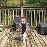 Elsie is registered to the contest to win money with this photo: toddler, child, deck, wooden_floor, sunglasses, pacifier, jacket, patterned_pants, outdoor_furniture, greenery, trees, house, railing, walking, sunny, daylight, casual_clothing, cute, baby, backyard