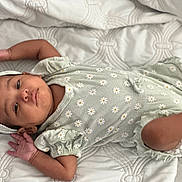 Amira joined the competition — help win amazing prizes! baby, infant, child, portrait, lying_down, indoors, bed, quilt, bonnet, dress, floral, daisies, patterned, face, eyes_open, skin, arms, legs, nursery, closeup