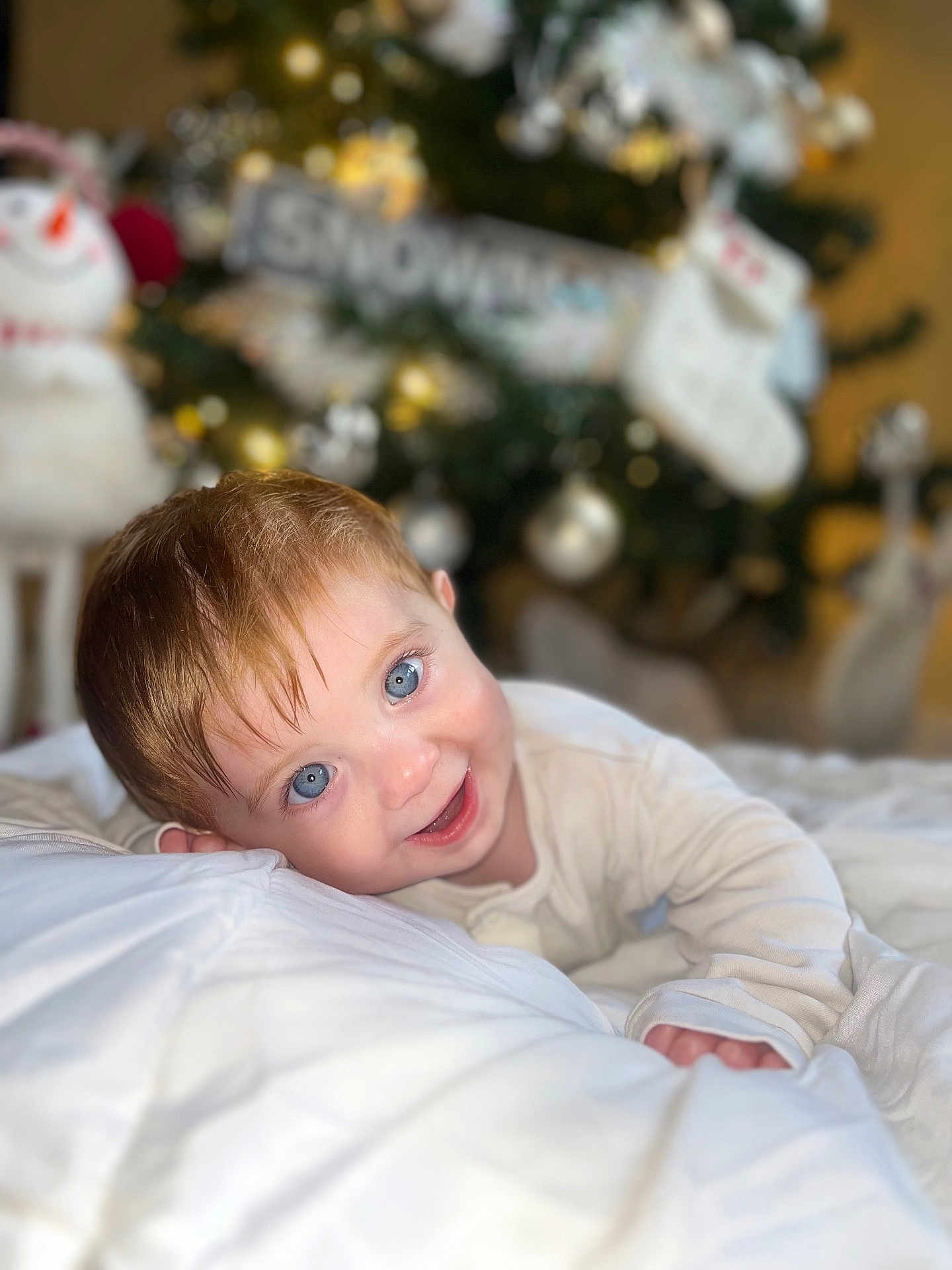 Dougie is registered to the contest to win money with this photo: toddler, baby, blue_eyes, smiling, white_blanket, christmas_tree, holiday, snowman, indoors, cute, portrait, child, soft_lighting, festive, cozy, happy, infant, face, expression, warm