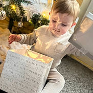 Theo joined the competition — help win amazing prizes! child, toddler, gift_box, christmas_tree, holiday, festive, ornaments, lights, indoors, carpet, pajamas, curious, present, decorations, face, young_child, holiday_season, warm_light, cozy, celebration