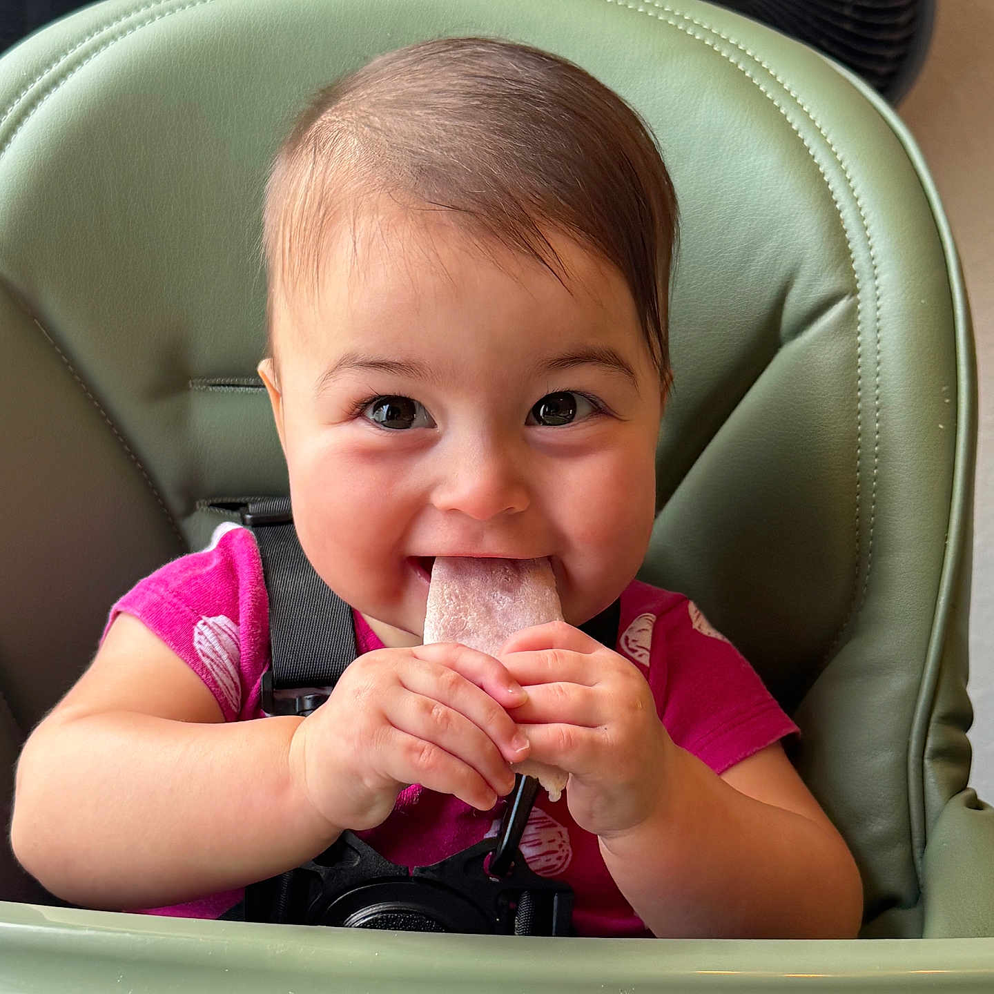 Eleanor is registered to the contest to win money with this photo: baby, child, high_chair, popsicle, smiling, happy, indoor, face, hands, food, cute, young_child, seat, clothing, pink_shirt, skin, hair, table, infant, playful