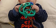 Noah a rejoint le concours — aidez-le/la à gagner de superbes lots ! baby, blue_outfit, child, clothing, cute, eyes, face, hand, head, indoor, infant, lying_down, orange_text, pacifier, person, pillow, skin, teething_toy, toy, young