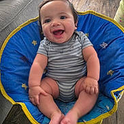 Archer is registered to the contest to win money with this photo: baby, smiling, child, blue_chair, striped_onesie, happy, indoor, wooden_floor, cushion, cute, infant, sitting, barefoot, person, young_child, comfort, playful, home, casual, relaxed