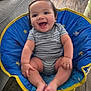 baby, smiling, child, blue_chair, striped_onesie, happy, indoor, wooden_floor, cushion, cute, infant, sitting, barefoot, person, young_child, comfort, playful, home, casual, relaxed