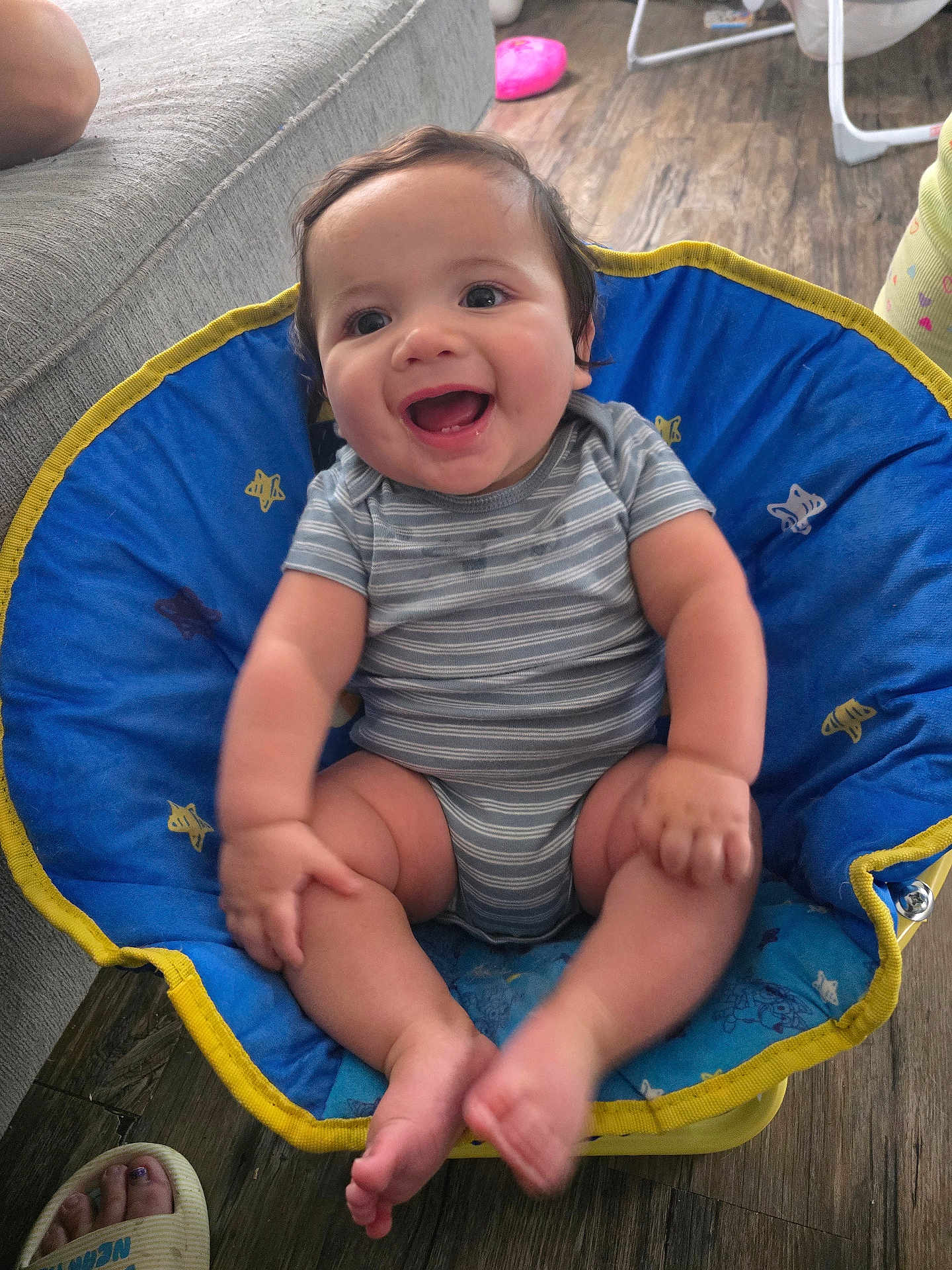Archer is registered to the contest to win money with this photo: baby, smiling, child, blue_chair, striped_onesie, happy, indoor, wooden_floor, cushion, cute, infant, sitting, barefoot, person, young_child, comfort, playful, home, casual, relaxed