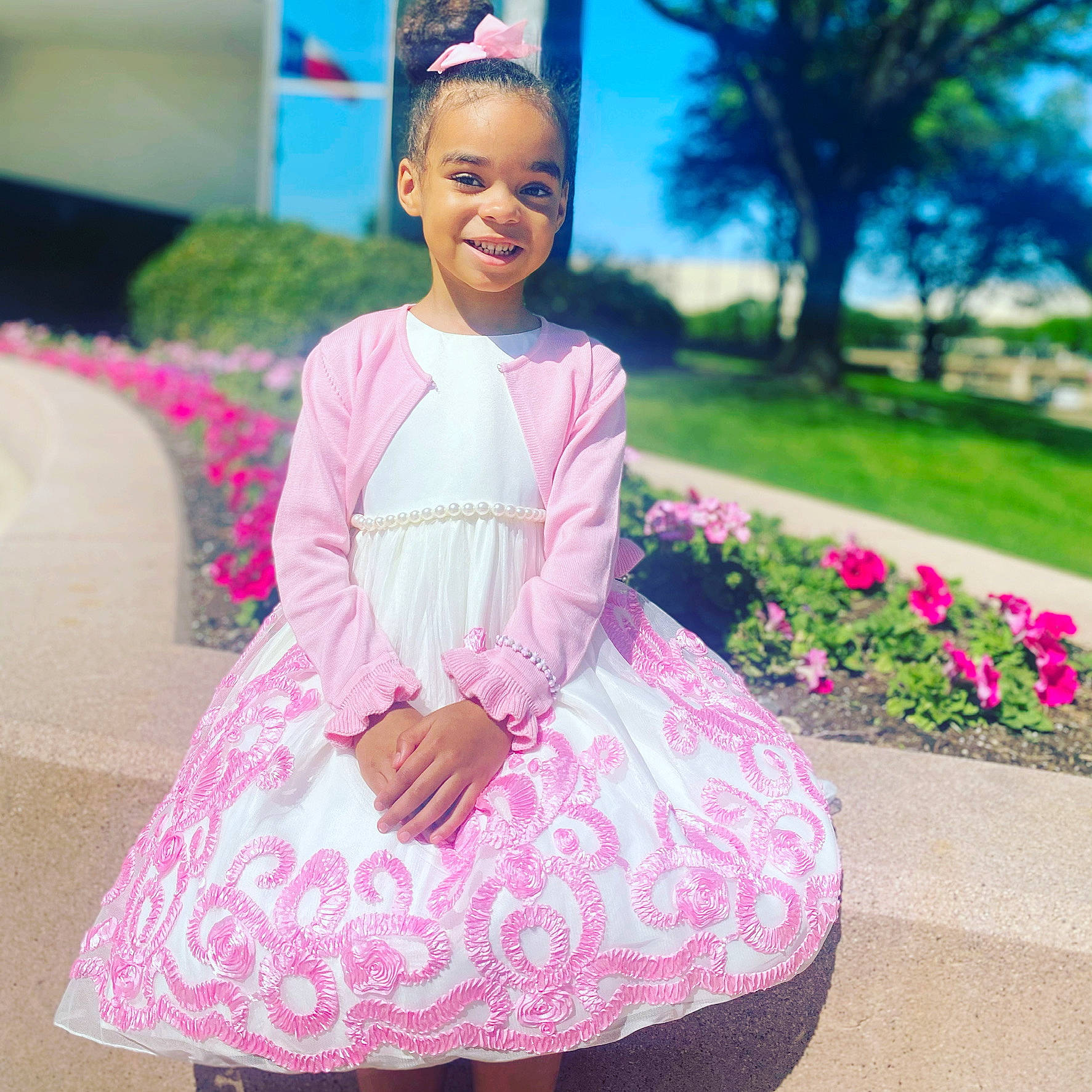 Brooklyn is registered to the contest to win money with this photo: baby_toddler_clothing, day_dress, dress, embellishment, event, flower, grass, happy, joy, leisure, magenta, outerwear, person, petal, pink, plant, recreation, sitting, sleeve, smile