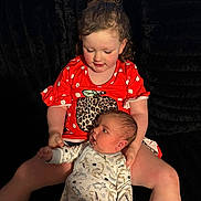 Bryson joined the competition — help win amazing prizes! toddler, baby, child, sibling, holding, red_shirt, polka_dot, onesie, dinosaur_pattern, curly_hair, seated, black_background, indoor, candid, family, cute, affection, portrait, soft_lighting, young