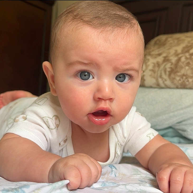 Jacob Rojas is registered to the contest to win money with this photo: baby, bed, blanket, blue_eyes, child, close_up, curious_expression, face, furniture, hand, head, indoor, infant, lying_down, mouth_open, pillow, portrait, skin, white_clothing, young_child