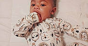 Amani joined the competition — help win amazing prizes! baby, child, infant, onesie, animal_print, hand_in_mouth, curly_hair, lying_down, white_background, quilted_bed, sleepwear, cute, portrait, indoors, small_child, face, expression, soft_lighting, comfortable, young