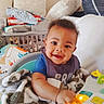 baby, blanket, child, clothing, colorful, cute, face, furniture, happy, home, indoor, infant, laundry_basket, light, pillow, playing, seated, smiling, toy, young_child