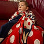 Lowen a rejoint le concours — aidez-le/la à gagner de superbes lots ! toddler, child, blanket, polka_dot, red_couch, seated, indoor, cozy, portrait, looking_away, furniture, home, soft_texture, comfort, young_child, casual, expression, couch, wrapped, relaxed