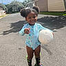 Aaliyah joined the competition — help win amazing prizes! child, toddler, smiling, volleyball, rain_boots, swimsuit, outdoor, street, sunny, suburban, puffy_hair, hair_buns, playful, happy, person, daylight, asphalt, tree, residential_area, sport