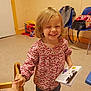 child, girl, smiling, holding_hand, book, indoor, toy, chair, playroom, casual_clothing, happy, person, blonde_hair, floor, wall, backpack, furniture, sleeves, young, cute