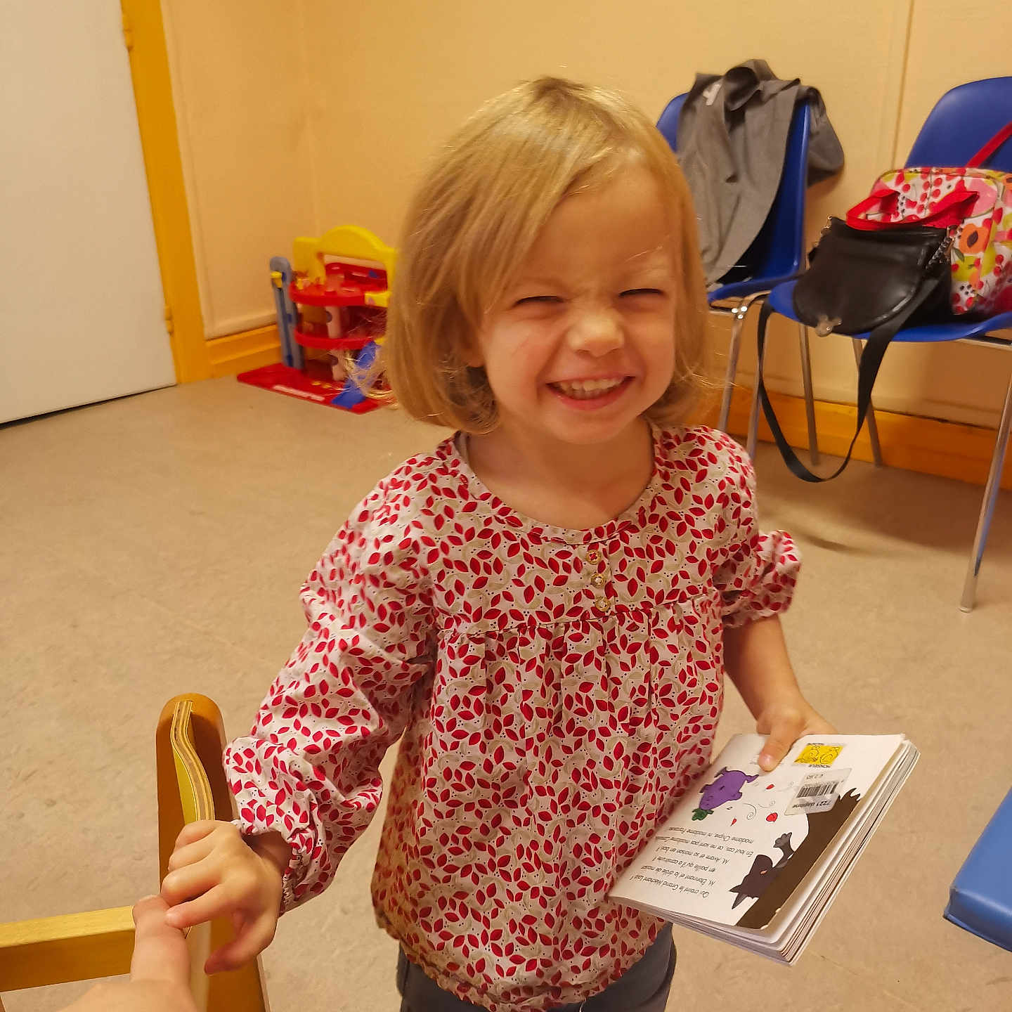 Santiana participe au concours pour gagner de l'argent avec cette photo : backpack, blonde_hair, book, casual_clothing, chair, child, cute, floor, furniture, girl, happy, holding_hand, indoor, person, playroom, sleeves, smiling, toy, wall, young
