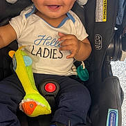 Kiel is registered to the contest to win money with this photo: baby, infant, car_seat, smiling, blue_shoes, plush_toy, white_shirt, sitting, happy, child, toy, footwear, indoor, clothing, cute, face, expression, seatbelt, accessory, head_support