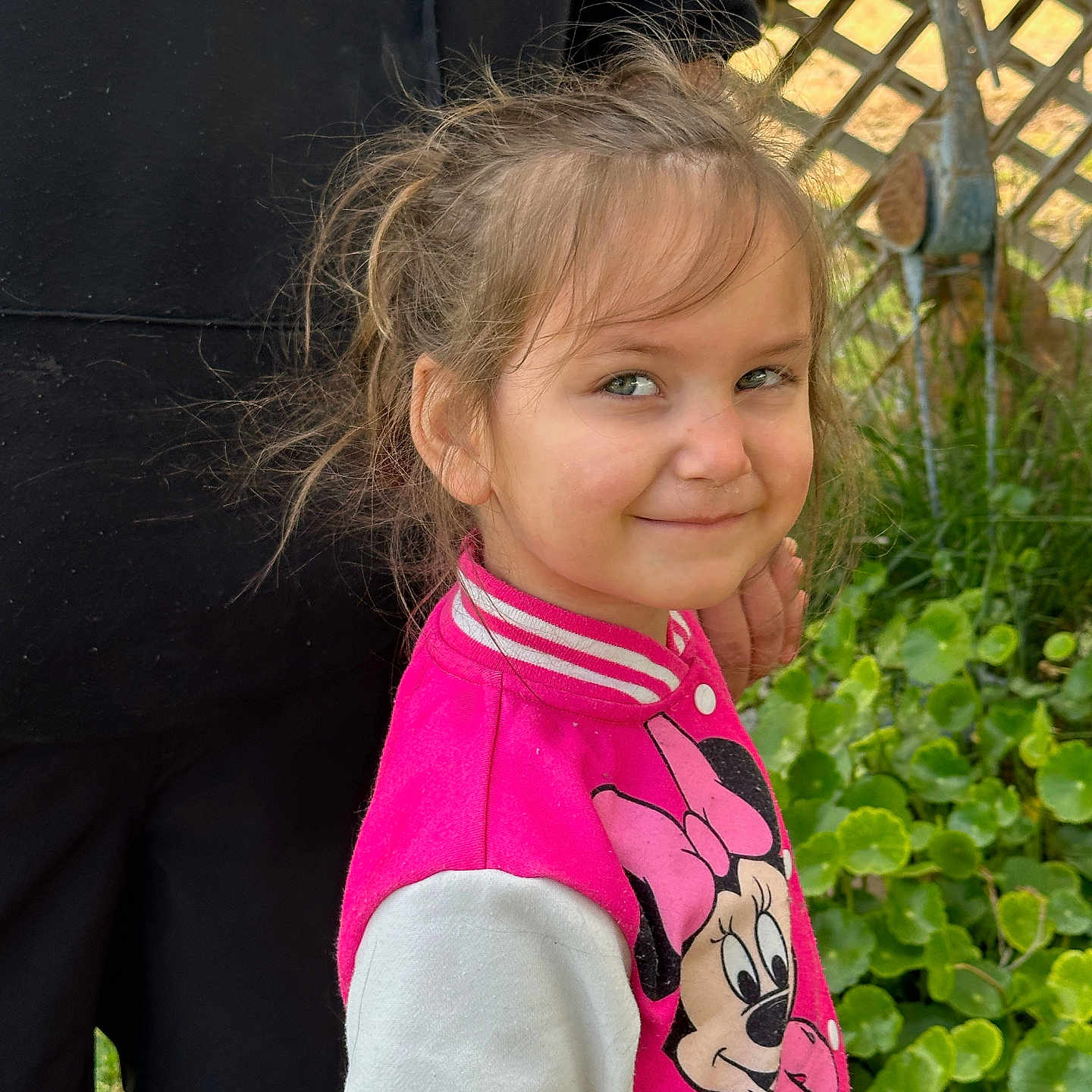 Kona is registered to the contest to win money with this photo: child, girl, smile, jacket, minnie_mouse, pink_clothing, outdoor, garden, greenery, fence, person, face, hair, expression, playful, casual, daylight, human, portrait, cute