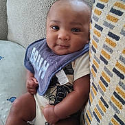 Jaiden joined the competition — help win amazing prizes! baby, infant, child, bib, couch, pillow, socks, clothing, smile, face, arm, leg, indoors, seated, cute, cozy, patterned_pillow, textile, skin, expression