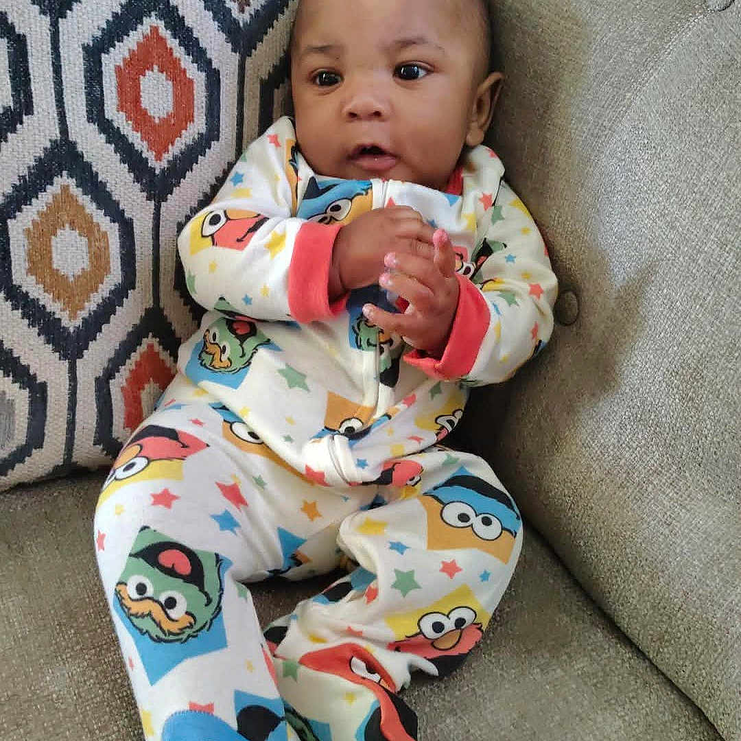 Jaiden joined the competition — help win amazing prizes! baby, infant, pajamas, colorful_clothing, couch, cushion, patterned_cushion, geometric_pattern, seated, indoors, child, clothing, cute, small_hands, curious_expression, home_interior, soft_furniture, portrait, child_in_pajamas, comfort