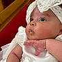baby, infant, white_dress, lace, pearls, closeup, chubby_cheeks, hand, cute, portrait, indoors, curious, gaze, soft_skin, headwear, bow, celebration, child, newborn, pink_skin