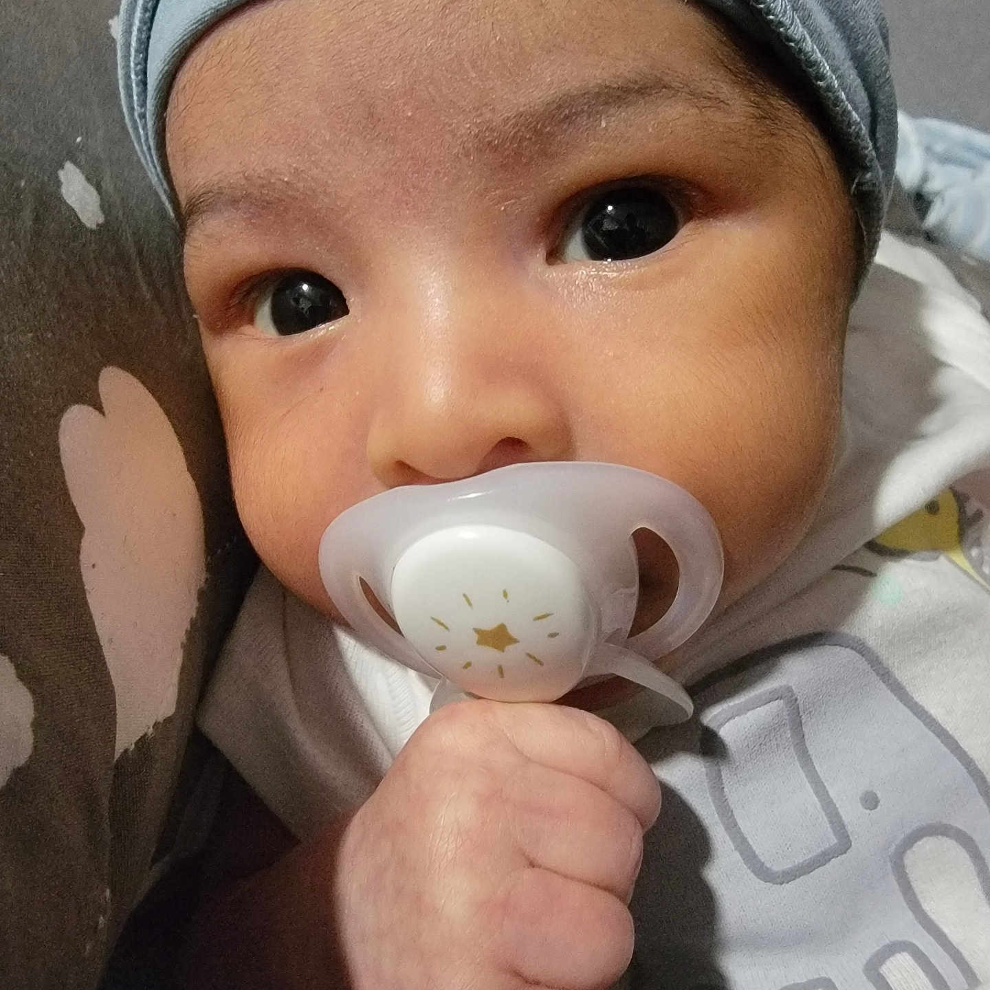 Eythan is registered to the contest to win money with this photo: baby, child, closeup, clothing, cozy, curious, cute, expression, face, hand, hat, holding, indoors, infant, newborn, pacifier, portrait, skin, sleepwear, young